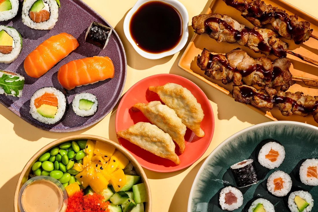 Maki and salmon nigiri, gyoza, chicken yakitori skewers and a poke bowl, photographed from above
